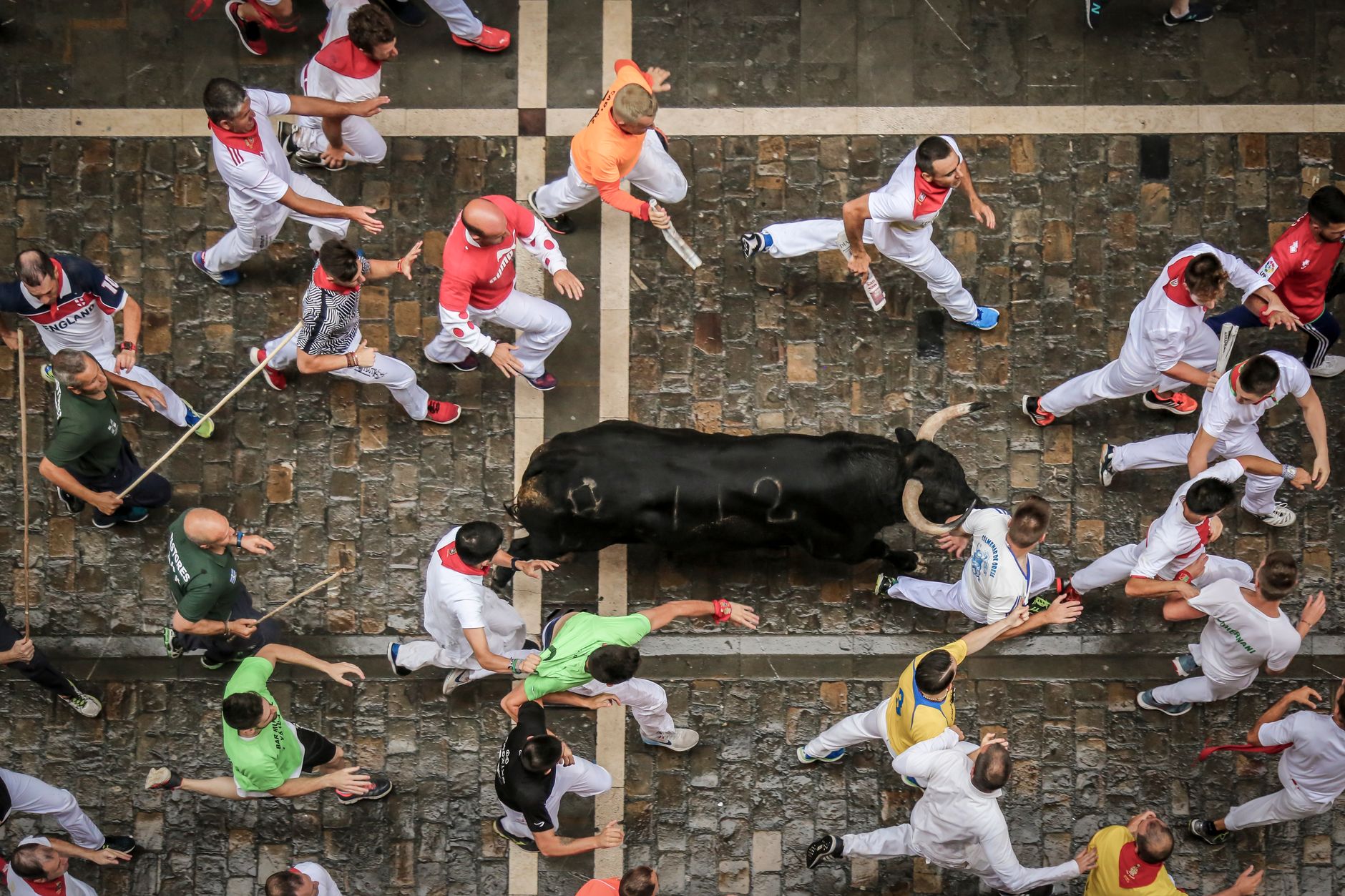 pamplona sanfermines white dressed runners with red scarves running from bulls through stone streets dramatic morning light